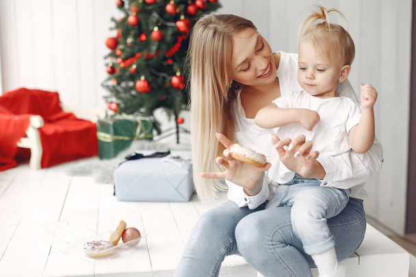 Mother with little daughter sitting near Christmas tree and and go donuts. - Foto, imagen