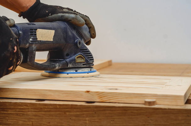 Schreinerwerkzeuge. Ein Holzbrett mit einem elektrischen Handschleifer schleifen - Foto, Bild