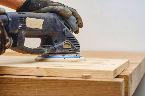 Joiner's tools. Sanding a wooden board with a hand-held electric sander - Zdjęcie, obraz