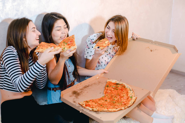 Χαριτωμένα κορίτσια δροσερό περνούν το χρόνο και να απολαύσετε πίτσα, να κάθονται στο πάτωμα στο φωτεινό υπνοδωμάτιο βράδυ. - Φωτογραφία, εικόνα