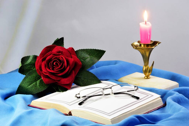 El libro está abierto con páginas en blanco y una rosa es la decoración de unas vacaciones creativas. Una vela vintage ilumina al autor. - Foto, Imagen