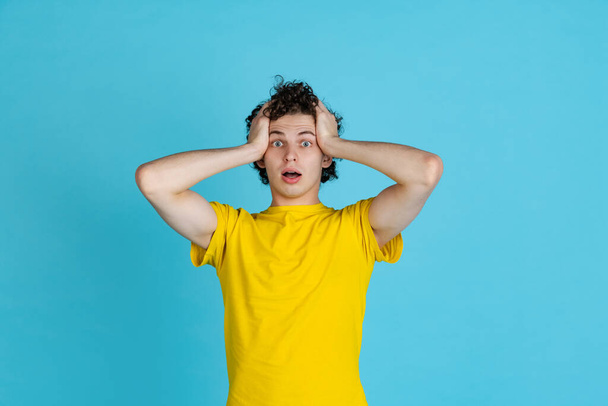 Cropped portrait of young man in yellow T-shirt touching forehead in shock isolated over blue background - Foto, Bild