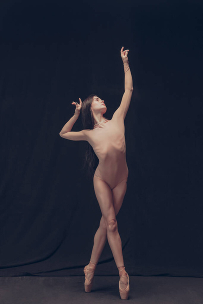Young flexible dancer, beautiful graceful woman in modern art performance isolated on black studio background. Art, motion, inspiration concept. - Fotó, kép
