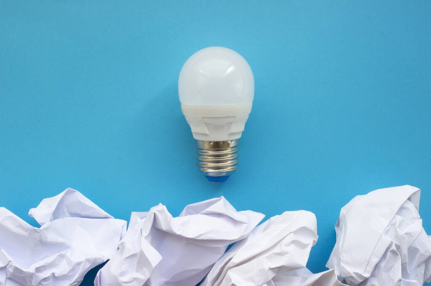 The concept of a brilliant idea. Creativity. Light bulb over crumpled paper. - Zdjęcie, obraz