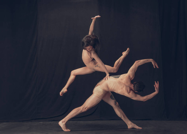Two flexible dancer, young man and woman in modern art performance isolated on black studio background. Art, motion, inspiration concept. - Photo, image