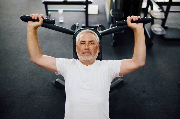 Oudere man, workout op fitnessapparaat, fitnessruimte - Foto, afbeelding