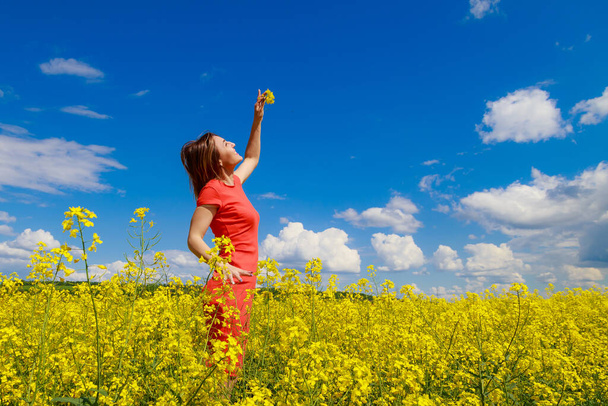 Young pretty woman in colored dress on lightning cheerful yellow background of blooming rapeseed field. Good mood concept - Photo, Image