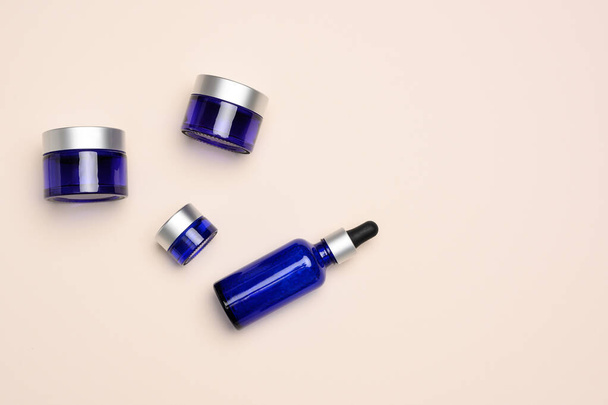 glass cosmetic blue bottles with a pipette  and jar on a beige background. Cosmetics SPA branding mockup, top view - 写真・画像