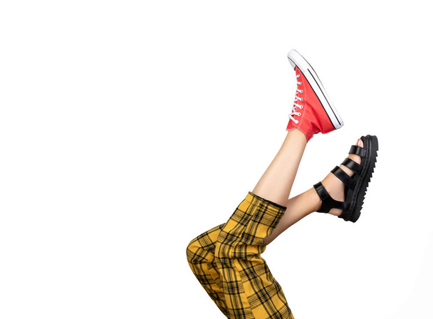 Gambe di una giovane donna in trendy scarpe da ginnastica rosse e sandali su sfondo bianco - Foto, immagini