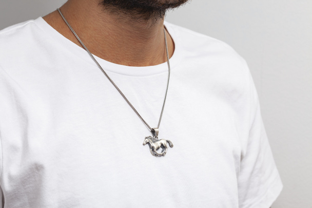 Modelo masculino joven en camiseta blanca posando con collar de plata sobre fondo suave.para compras en línea. - Foto, imagen