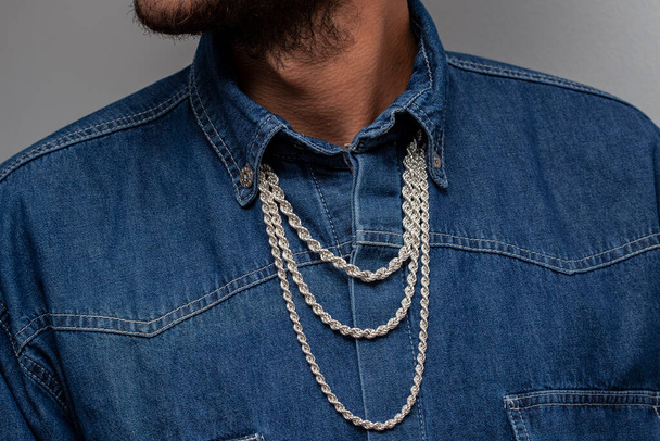 Young male model in a white t-shirt and blue denim shirt poses with silver chains. - 写真・画像