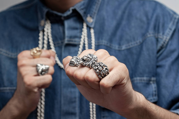Young male model in a white t-shirt and blue denim shirt poses with a silver ring and silver chains. - Фото, зображення