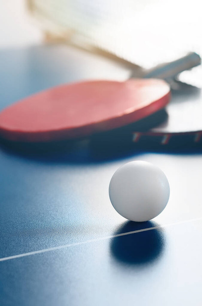 Deux raquettes de tennis et une balle blanche reposent sur une table de tennis près du filet. Loisirs actifs et jeu de ping-pong. - Photo, image