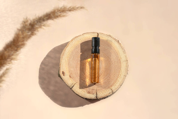 Probador de perfumes con líquido marrón transparente en un corte de madera con hierba de pampas sobre fondo beige - Foto, Imagen