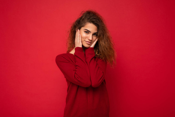 Kendine güveni tam kıvırcık, esmer, samimi duyguları olan genç bir kadın arka plan duvarında izole edilmiş koyu kırmızı süveter giyiyor. Pozitif kavram - Fotoğraf, Görsel