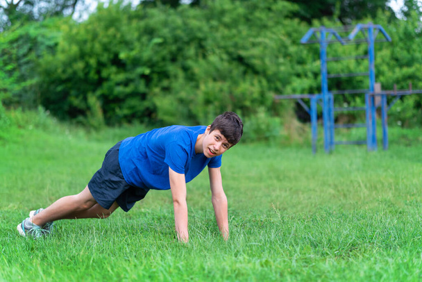 teenage boy exercising outdoors, sports ground in the yard, he squats and does a warm-up, healthy lifestyle - Foto, Imagen