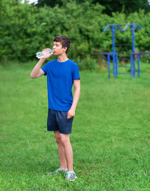 Jugendlicher beim Sport im Freien, Sportplatz im Hof, er öffnet eine Flasche Wasser und Getränke, gesunder Lebensstil - Foto, Bild