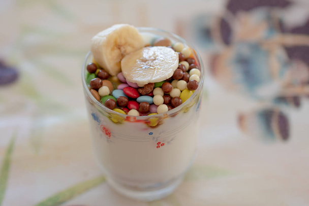 επιδόρπιο γαλακτοκομικό με φρούτα, δημητριακά και σοκολάτα σε κρυστάλλινο ποτήρι διακοσμημένο με φυτικά σχέδια - Φωτογραφία, εικόνα