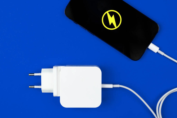 Φορτιστής Lightning. Smartphone με ενεργειακό εικονίδιο και φορτιστή ρεύματος σε μπλε φόντο. Πάνω άποψη, επίπεδη lay  - Φωτογραφία, εικόνα
