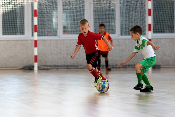 OESSA, UKRAINE - 10月14, 2021:小さな男の子8-9年,子供たちは、ウクライナ選手権でスポーツホールでミニサッカーをプレイ.子供のスポーツは健康的なライフスタイルです。少年スポーツサッカー選手フットサル - 写真・画像