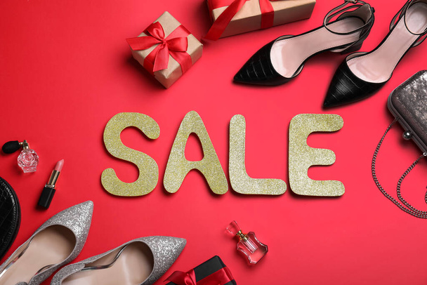 Word Sale made of golden letters near gift boxes, women's shoes and accessories on red background, flat lay. Black Friday - Foto, Bild