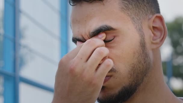 Primo piano ritratto di stanco sconvolto triste giovane uomo arabo mediorientale strofinando ponte di naso. Millennial ragazzo indiano studente tocca il viso, vuole dormire, sente tensione, mal di testa, affaticamento degli occhi, ha bisogno di riposo - Filmati, video