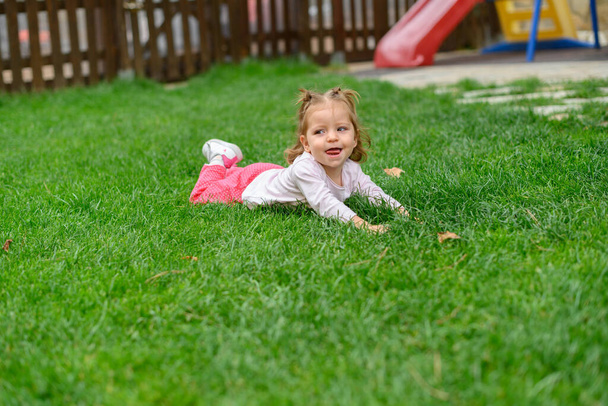 Portret van een meisje dat op het gras ligt en lacht op de speelplaats - Foto, afbeelding