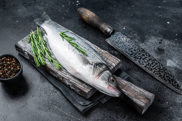 Verse Rauwe zeebaars of zeebaars vis op een houten plank klaar om te koken. Zwarte achtergrond. Bovenaanzicht - Foto, afbeelding