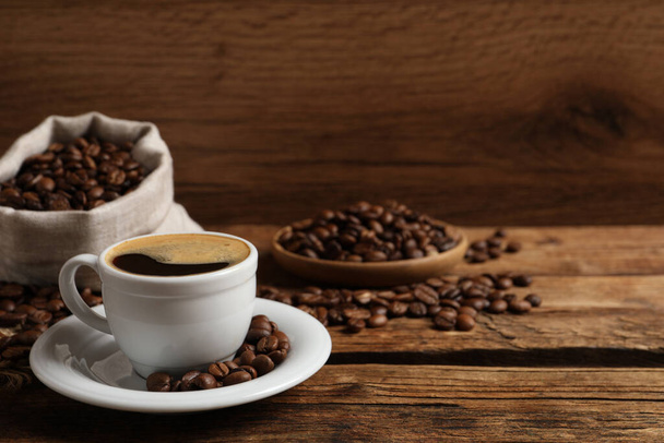 Filiżanka aromatycznej gorącej kawy i fasoli na drewnianym stole, miejsce na tekst - Zdjęcie, obraz