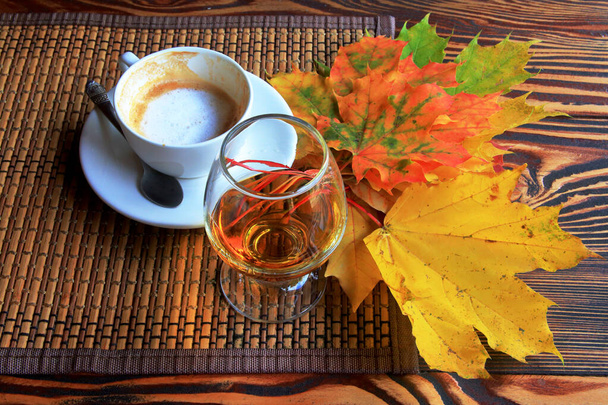 la photo montre une nature morte d'automne avec une tasse de café, un verre de brandy et des feuilles lumineuses. - Photo, image