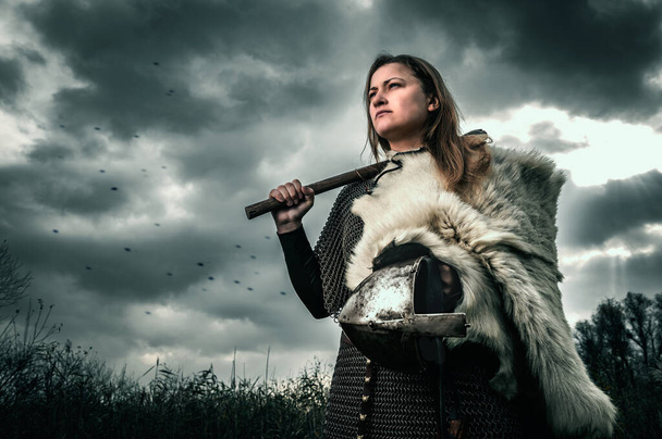 Portrait of woman in image of medieval warrior under dramatic sky. Beautiful woman in medieval chain mail - Photo, Image