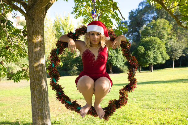lihava blondi nainen ja antenni vanne urheilija pukeutunut joulupukki tekee erilaisia akrobaattisia asentoja onnitella joulua. Käsite urheilu ja joulu. - Valokuva, kuva