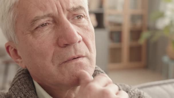 Detailní záběr zamyšleného staršího bělocha sedícího v obývacím pokoji, přemýšlejícího a hledícího do dálky, dotýkajícího se rukou obličeje - Záběry, video