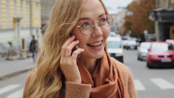 Close-up emotional young millennial girl talking on telephone outdoor caucasian female enjoys pleasant mobile conversation portrait of beautiful smiling woman speaking on phone actively gesticulates - Footage, Video