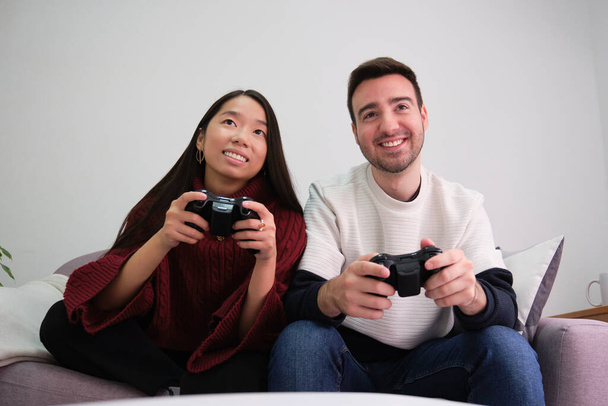 Nuori monirotuinen pari pelaa videopelejä ja käyttää joystick ohjaimet. - Valokuva, kuva