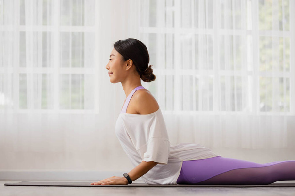 Asian woman practising yoga, Cobra exercise, Bhujangasana stance, working out, and wearing sportswear. - Photo, Image