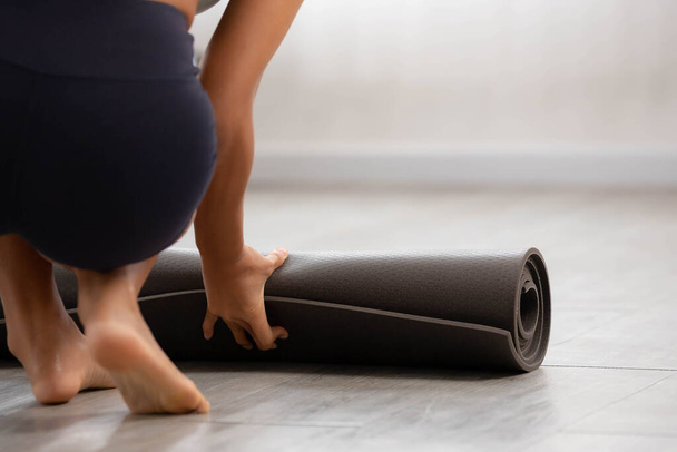 Gros plan mains d'une femme asiatique sont enrouler un tapis d'exercice et se préparer à conduire le yoga. Elle fait de l'exercice à la maison sur un tapis de sol au début du soleil. - Photo, image