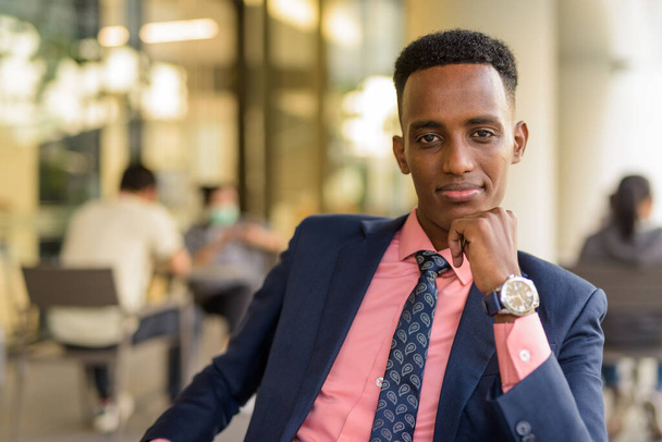 コーヒーショップでスーツを着て屋外でネクタイをしている若いアフリカ人ビジネスマンの肖像 - 写真・画像