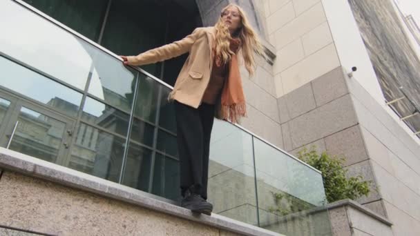 Dolny widok stylowe piękne młoda dziewczyna stać na tarasie w pobliżu biurowca zamyślony kobieta pochylił się do przodu i podnieść głowę w górę trzymając balkon szyna kaukaski biznes kobieta korzystających odpoczynku na zewnątrz - Materiał filmowy, wideo