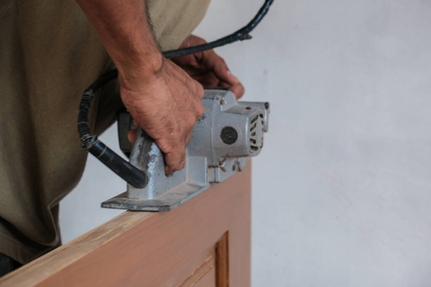 Mão de carpinteiro trabalhando com plaina elétrica na porta de madeira de teca na oficina. - Foto, Imagem