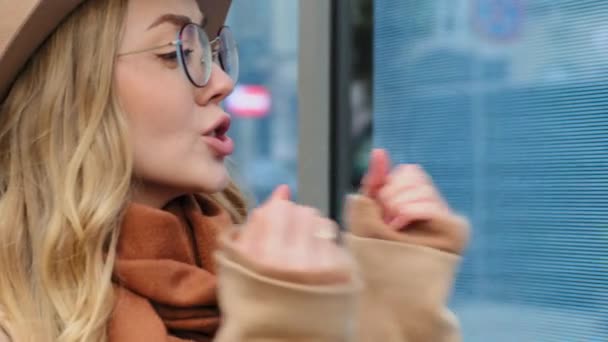 Verrast jong mooi vrouw buiten emotioneel meisje in hoed en bril gelukkig springen verbaasd opgewonden dame gevoel vreugde Kaukasisch vrouw actief gesticuleren handen krullend blond walkin op straat - Video