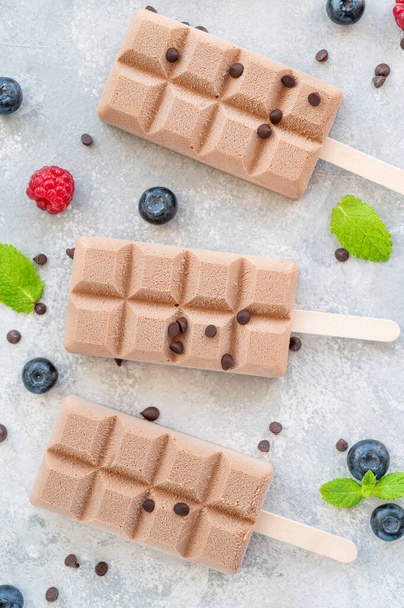 Zelfgemaakt chocolade-ijs (ijslolly 's) met verse frambozen en bosbessen op een grijze achtergrond. kopieerruimte - Foto, afbeelding