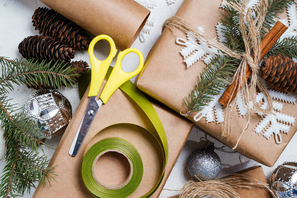 Papel artesanal con cinta verde y tijeras. Hacer arco en la caja de regalo de Navidad, decorado con copo de nieve en la mesa blanca, vista superior. - Foto, Imagen