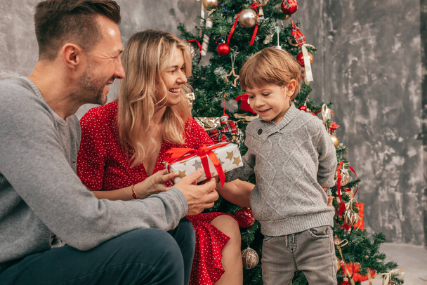 Photo of Dad, mom and son. Spending time together. Christmas tree at home, happy moments. Preparing for holiday. Happy together. Have fun with gift box. Red green colors. New Year eve - Photo, Image