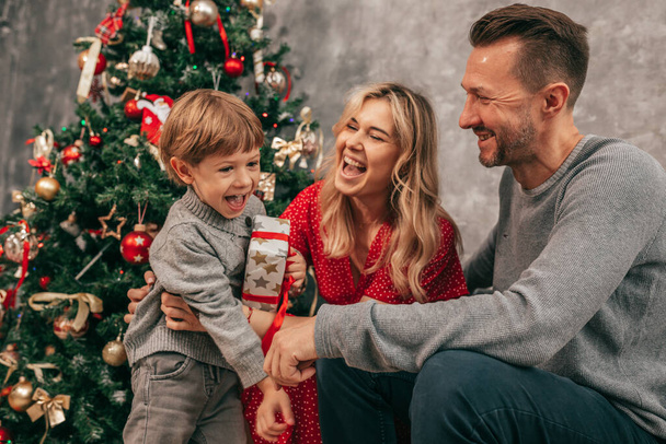 Photo of Dad, mom and son. Spending time together. Christmas tree at home, happy moments. Preparing for holiday. Family with one child. Happy together. Have fun with gift box. - Фото, зображення