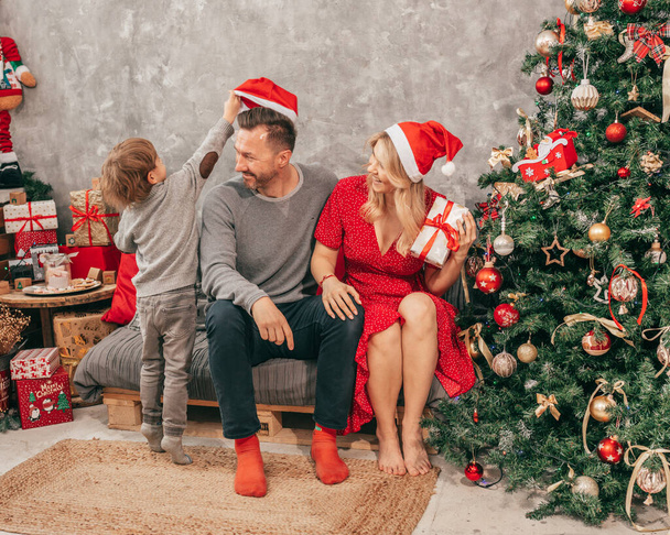 パパとママと息子の写真。時間を使って。家でクリスマスツリー、幸せな瞬間。休暇の準備だ。1人の子供を持つ家族。一緒に幸せだ。ギフトボックスでお楽しみください. - 写真・画像