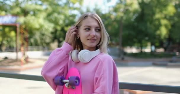 Γυναίκα με ακουστικά και penny board χαλαρώνει στο πάρκο - Πλάνα, βίντεο