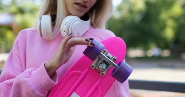 Nuori blondi nainen leikkii penniäkään hallituksen pyörät puistossa - Materiaali, video