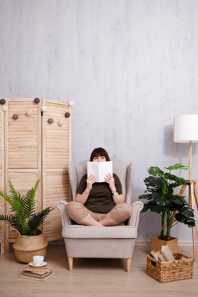 Shy woman covering her face with book and dreaming at home - Фото, изображение