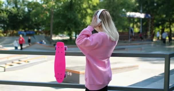 Lady walks with penny board listening to music in headphones - Footage, Video